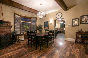 Dining area featuring beam ceiling, a chandelier, a fireplace, and dark wood-type flooring