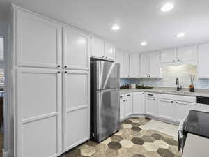 Kitchen with stainless steel fridge, tasteful backsplash, sink, white cabinets, and range