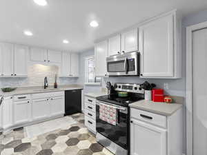 Kitchen with white cabinets, decorative backsplash, stainless steel appliances, and sink