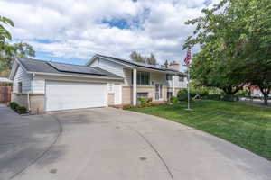 View of front of property featuring a front lawn, a garage, and solar panels