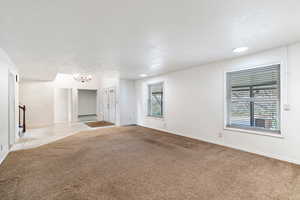 Carpeted empty room with a textured ceiling and an inviting chandelier