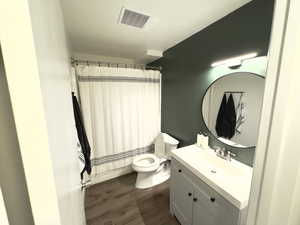 Bathroom with wood-type flooring, vanity, toilet, and curtained shower