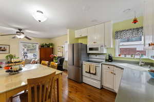 Kitchen with white appliances, sink, ceiling fan, dark hardwood / wood-style flooring, and white cabinetry