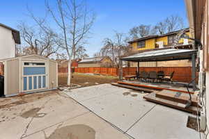 View of patio with a gazebo, a wooden deck, and a storage unit