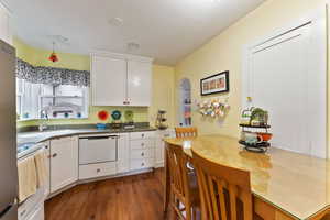 Kitchen featuring dark wood-type flooring, sink, dishwasher, white cabinets, and range