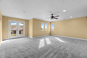 Carpeted empty room with ceiling fan, a healthy amount of sunlight, a textured ceiling, and french doors