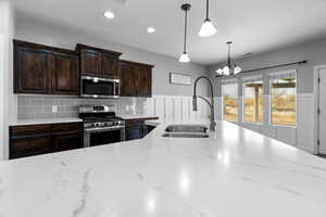 Kitchen featuring sink, light stone counters, backsplash, pendant lighting, and appliances with stainless steel finishes