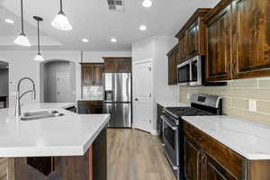 Kitchen featuring sink, an island with sink, decorative light fixtures, dark brown cabinets, and stainless steel appliances