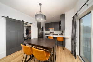 Kitchen with a barn door, range hood, kitchen peninsula, light LVP floors, and appliances with stainless steel finishes