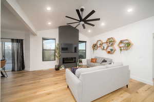 Living room featuring a large fireplace, light LVP floors, ceiling fan, and lofted ceiling