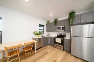 Kitchen with gray cabinetry, light LVP floors, sink, and appliances with stainless steel finishes