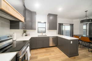 Kitchen with sink, light LVP flooring, kitchen peninsula, appliances with stainless steel finishes, and custom exhaust hood