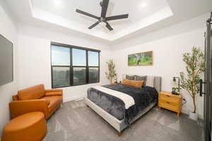 Carpeted bedroom with a raised ceiling and ceiling fan