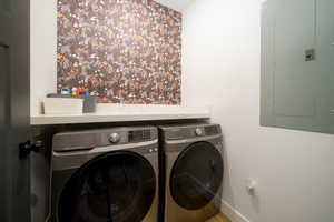 Clothes washing area featuring electric panel and washing machine and clothes dryer