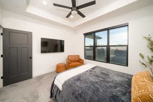 Carpeted bedroom with a raised ceiling and ceiling fan