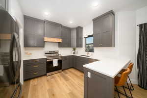 Kitchen with a kitchen bar, appliances with stainless steel finishes, light LVP flooring, kitchen peninsula, and gray cabinetry