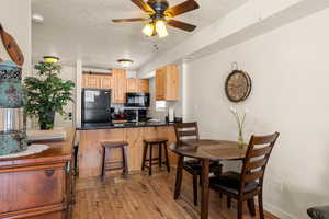 Kitchen with kitchen peninsula, a kitchen breakfast bar, a textured ceiling, black appliances, and light hardwood / wood-style floors