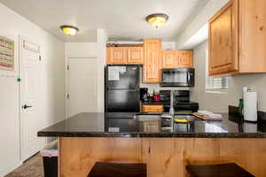 Kitchen featuring kitchen peninsula, a textured ceiling, a breakfast bar area, light tile patterned floors, and black appliances