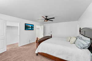 Bedroom featuring ceiling fan, a textured ceiling, a walk in closet, light carpet, and a closet