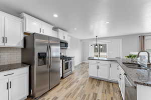 Kitchen with hanging light fixtures, white cabinetry, appliances with stainless steel finishes, and sink