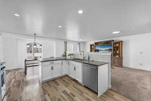 Kitchen with sink, dark stone countertops, white cabinets, decorative light fixtures, and stainless steel dishwasher