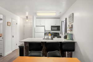 Kitchen featuring black appliances, white cabinets, sink, light hardwood / wood-style floors, and kitchen peninsula