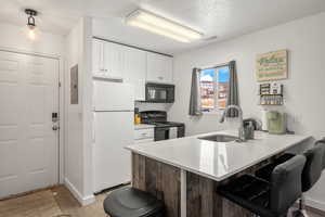 Kitchen featuring black appliances, white cabinets, sink, decorative light fixtures, and kitchen peninsula