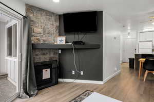 Living room featuring a stone fireplace, ceiling fan, light hardwood / wood-style flooring, and a textured ceiling