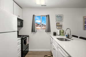 Kitchen featuring black appliances, sink, a textured ceiling, light hardwood / wood-style floors, and white cabinetry