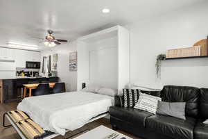 Bedroom with a textured ceiling, white refrigerator, ceiling fan, and dark wood-type flooring