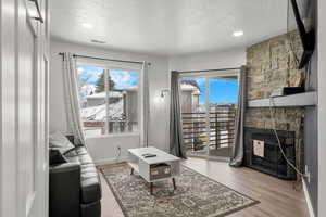 Living room with light hardwood / wood-style floors, a stone fireplace, and a textured ceiling