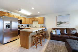 Kitchen with stainless steel appliances, sink, light tile patterned floors, tile countertops, and a breakfast bar area