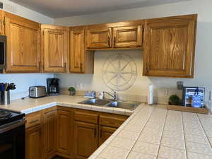 Kitchen with range with electric cooktop, sink, and tile countertops