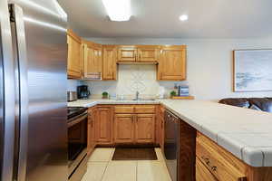 Kitchen featuring kitchen peninsula, stainless steel appliances, sink, light tile patterned floors, and tile countertops