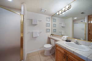 Bathroom featuring tile patterned flooring, vanity, a shower with door, and a textured ceiling