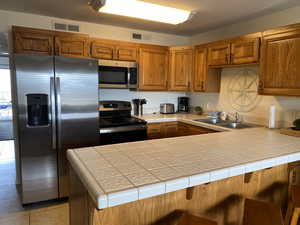 Kitchen featuring sink, tile countertops, light tile patterned floors, appliances with stainless steel finishes, and kitchen peninsula