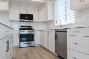 Kitchen featuring decorative backsplash, appliances with stainless steel finishes, sink, white cabinets, and light hardwood / wood-style floors