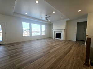 Unfurnished living room with a tile fireplace, dark hardwood / wood-style floors, ceiling fan, and a tray ceiling