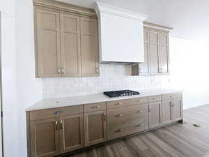 Kitchen with light wood-type flooring, stainless steel gas stovetop, and backsplash