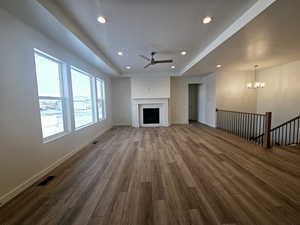 Unfurnished living room with wood-type flooring, ceiling fan with notable chandelier, and a tray ceiling