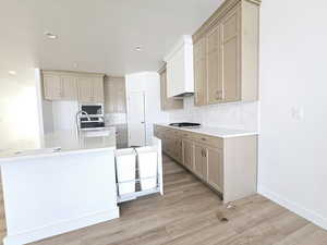 Kitchen with sink, stainless steel appliances, light hardwood / wood-style flooring, backsplash, and an island with sink