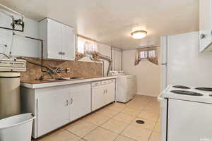 Kitchen with white appliances, backsplash, white cabinetry, and washing machine and clothes dryer