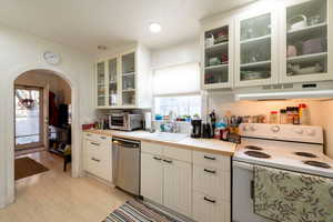 Kitchen with light wood-type flooring, sink, dishwasher, white range with electric cooktop, and white cabinetry