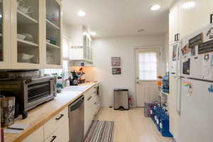 Kitchen with light wood-type flooring, stainless steel dishwasher, sink, white refrigerator, and white cabinetry