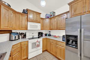 Kitchen featuring sink, white appliances, lofted ceiling, and light tile patterned flooring