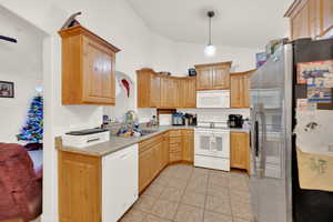 Kitchen with pendant lighting, white appliances, sink, vaulted ceiling, and light tile patterned floors