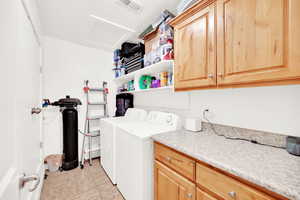 Clothes washing area with washing machine and clothes dryer, light tile patterned floors, and cabinets