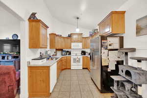 Kitchen with pendant lighting, white appliances, sink, vaulted ceiling, and light tile patterned flooring