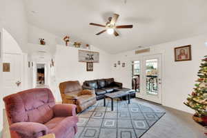 Living room with ceiling fan, light colored carpet, and vaulted ceiling