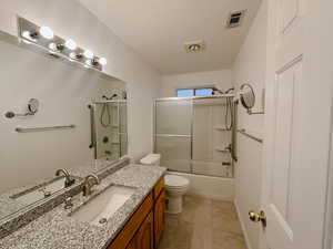 Full bathroom featuring vanity, bath / shower combo with glass door, tile patterned flooring, toilet, and a textured ceiling